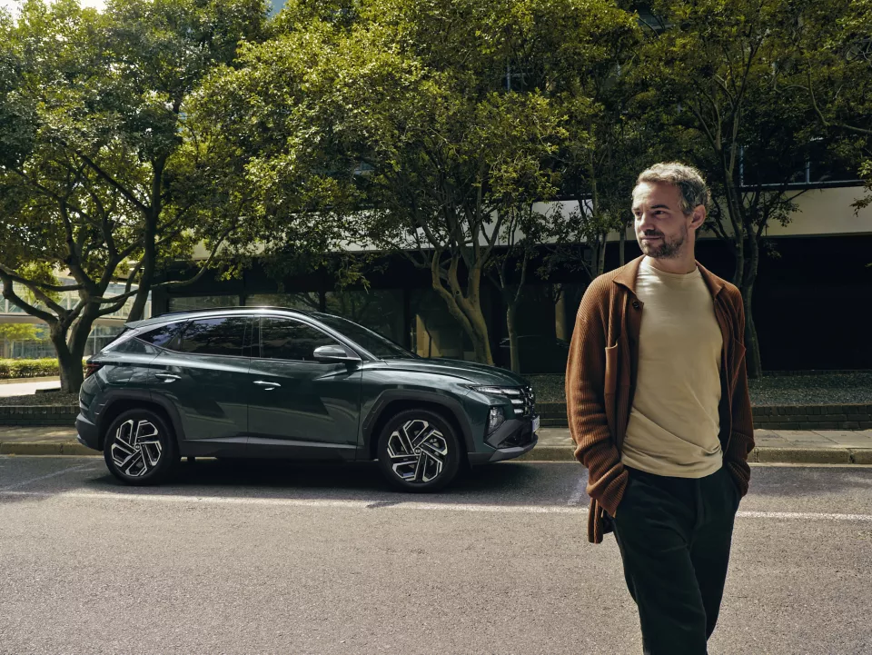 The Hyundai TUCSON Plug-in Hybrid parked on a tree-lined street with a man walking away from it.